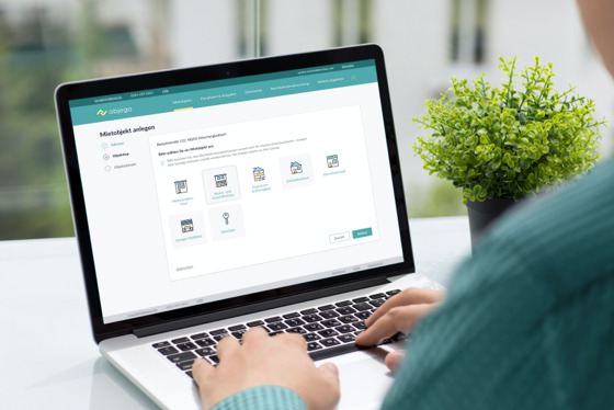 Person in Pullover sitzt an einem Laptop neben einer Pflanze. Der Bildschirm zeigt den Bereich Mietobjekte anlegen der objego Software.