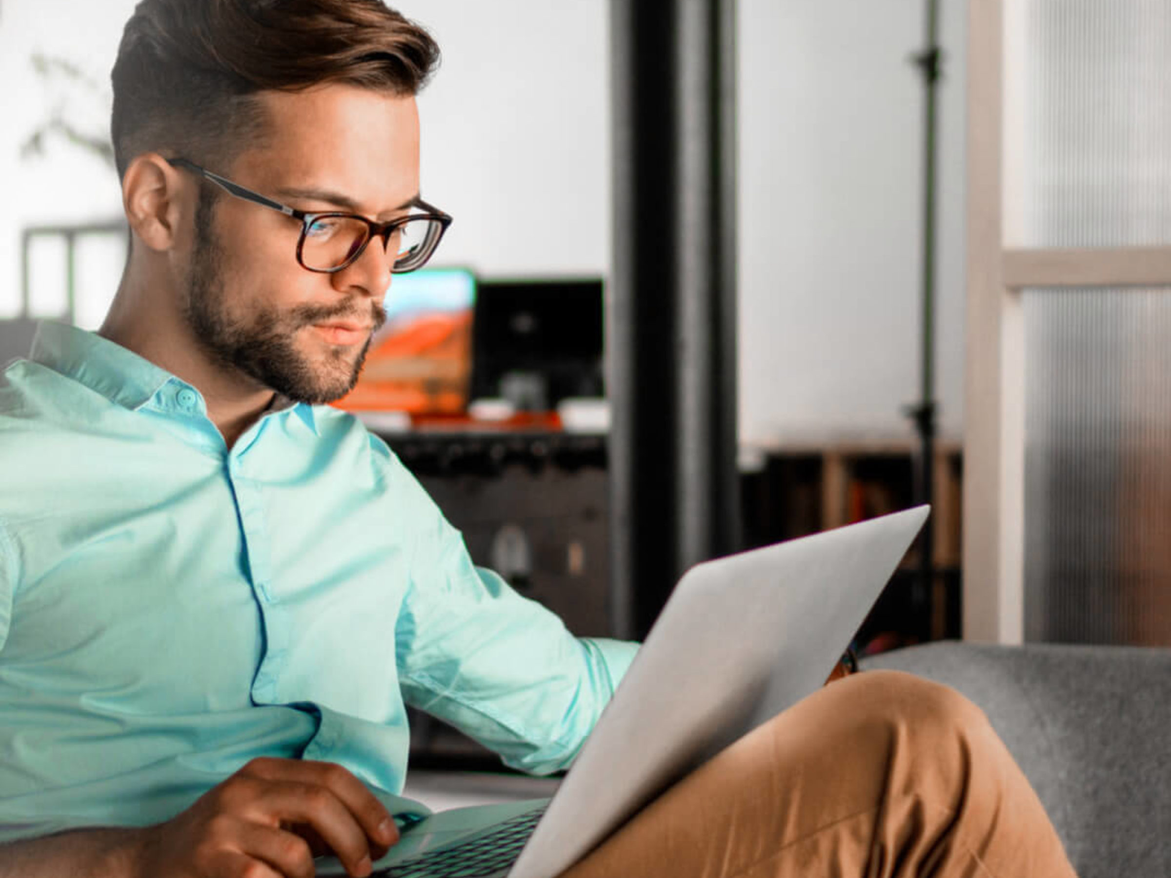 Mann hat einen Laptop auf dem Schoss und schaut sich auf dem Bildschirm etwas an.