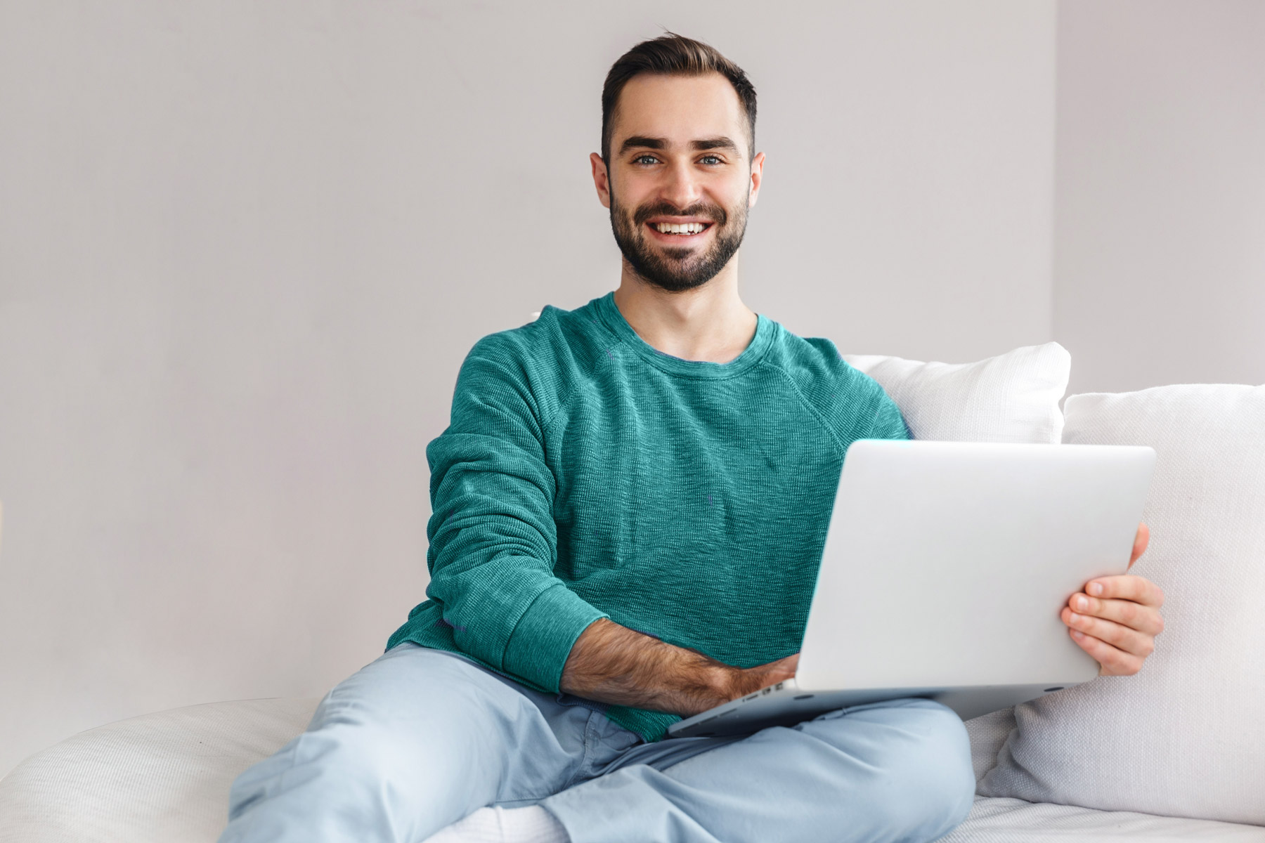 Mietpreisrechner: Mann sitzt auch Couch und hat einen Laptop auf seinem Bein. Er laechelt in die Kamera.